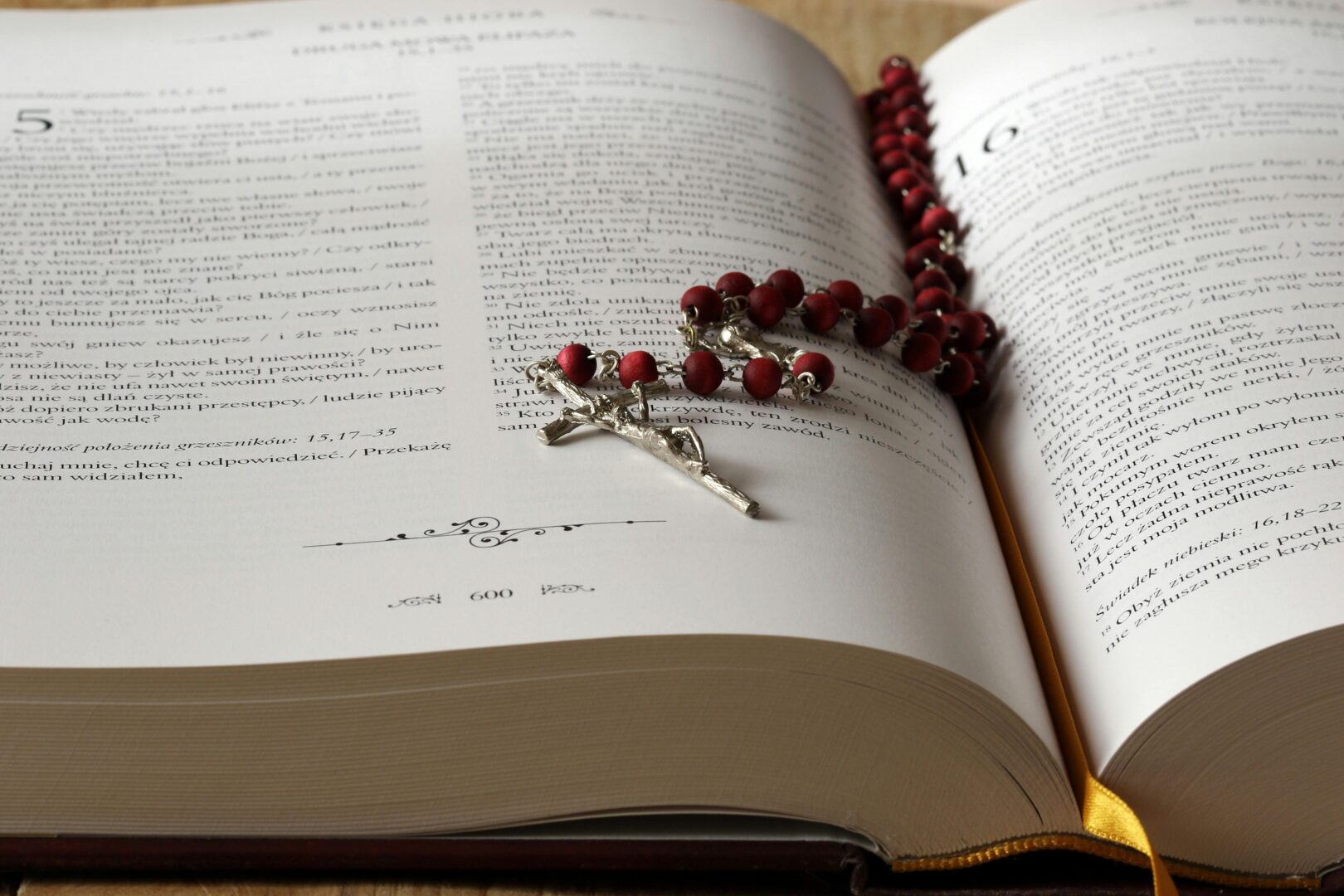 Open Bible with red rosary beads draped on pages, symbolizing faith and devotion.